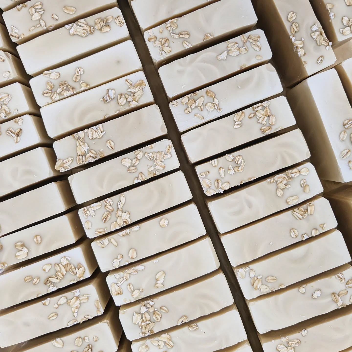 Rows of beige soap bars with oats decoratively placed on top of each bar