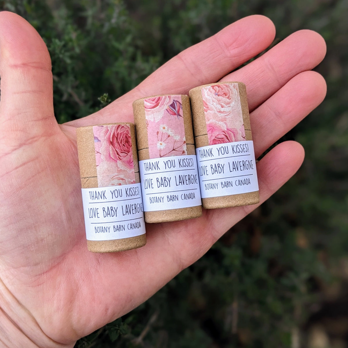 Three lip balms with floral decal, held in a hand