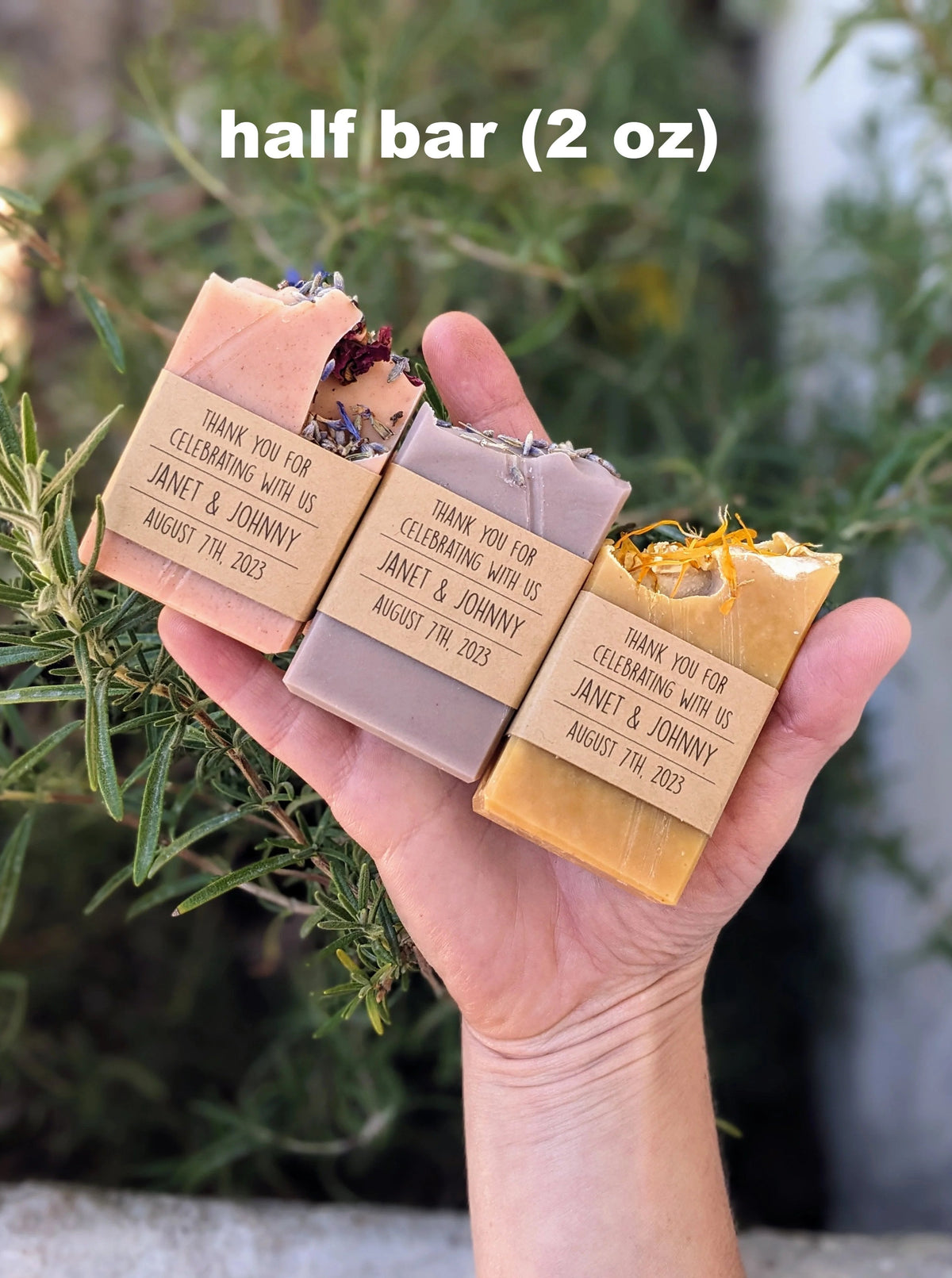 Three handmade soap bars held in a hand, wrapped in brown kraft paper with customized labels.