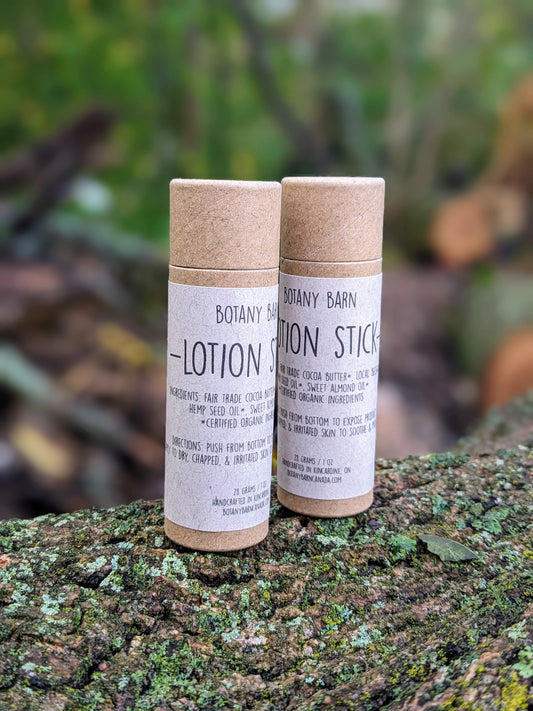 Two solid lotion sticks placed on a natural wood surface, with labels indicating the Botany Barn brand and ingredients.