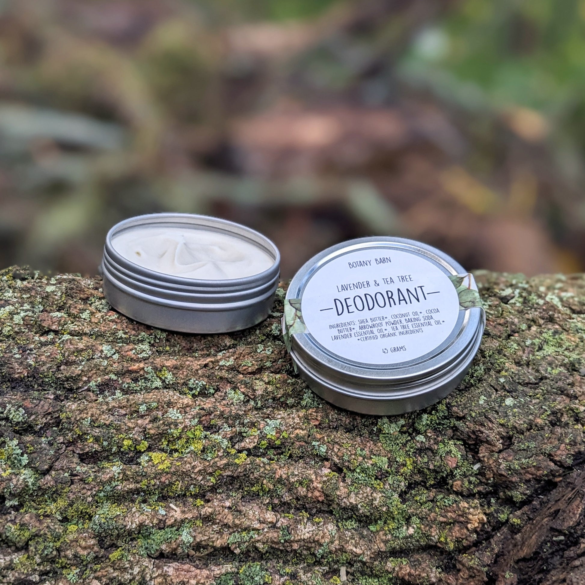 A small metal tin deodorant container, open, showing the solid white deodorant inside, placed on a natural wood surface.