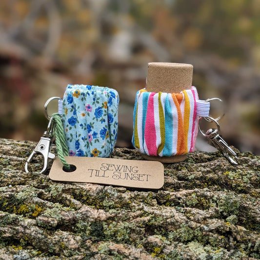 Two lip balm holders attached to keychains, one floral and one striped, displayed on a wooden surface.