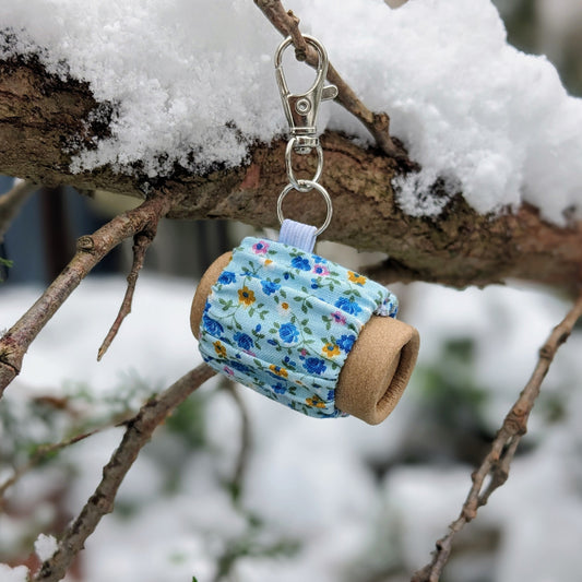 A lip balm is contained inside a piece of floral fabric, hanging on a keychain
