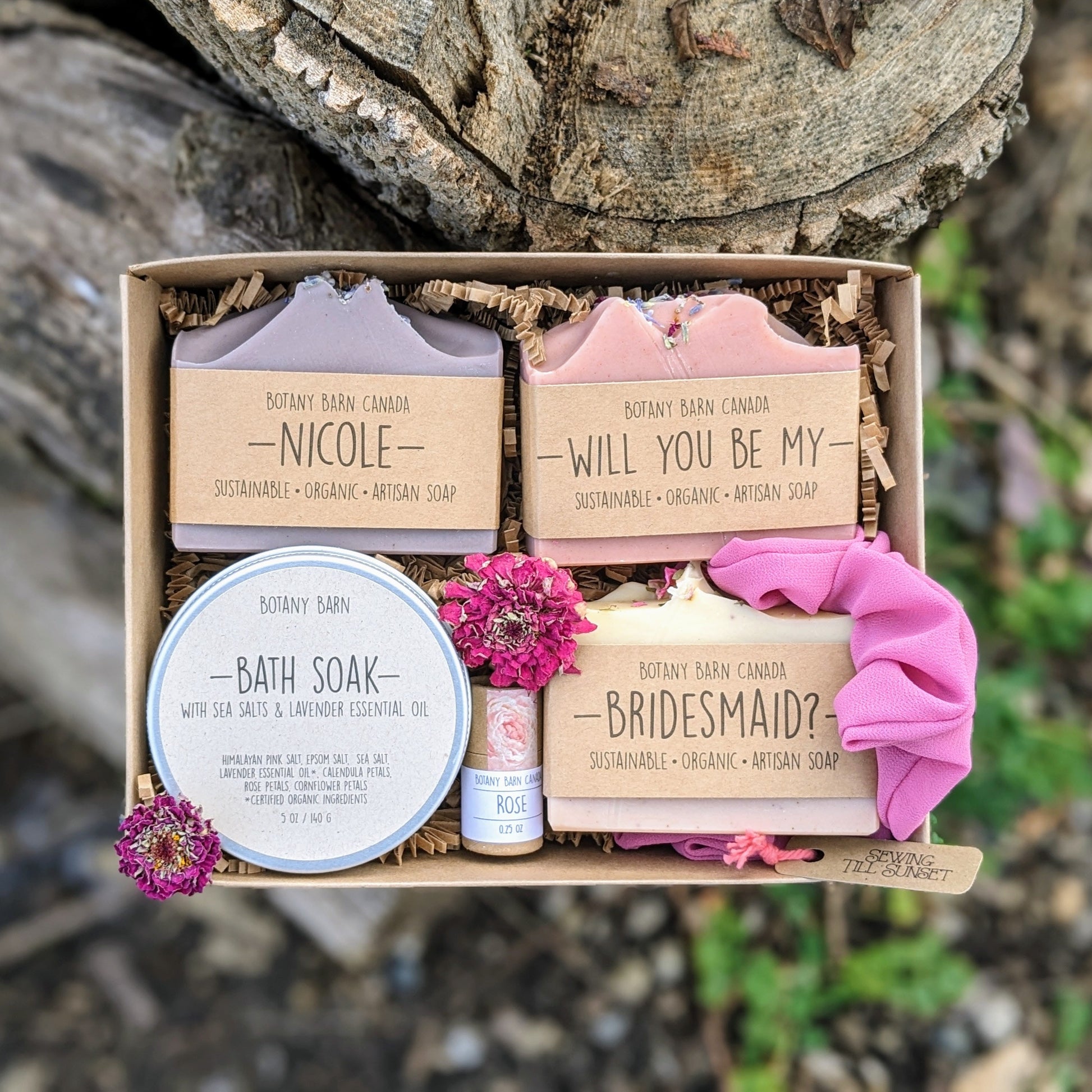 A gift set including soap bars, bath salts, lip balm and scrunchie. Custom soap labels read: Nicole, will you be my bridesmaid?
