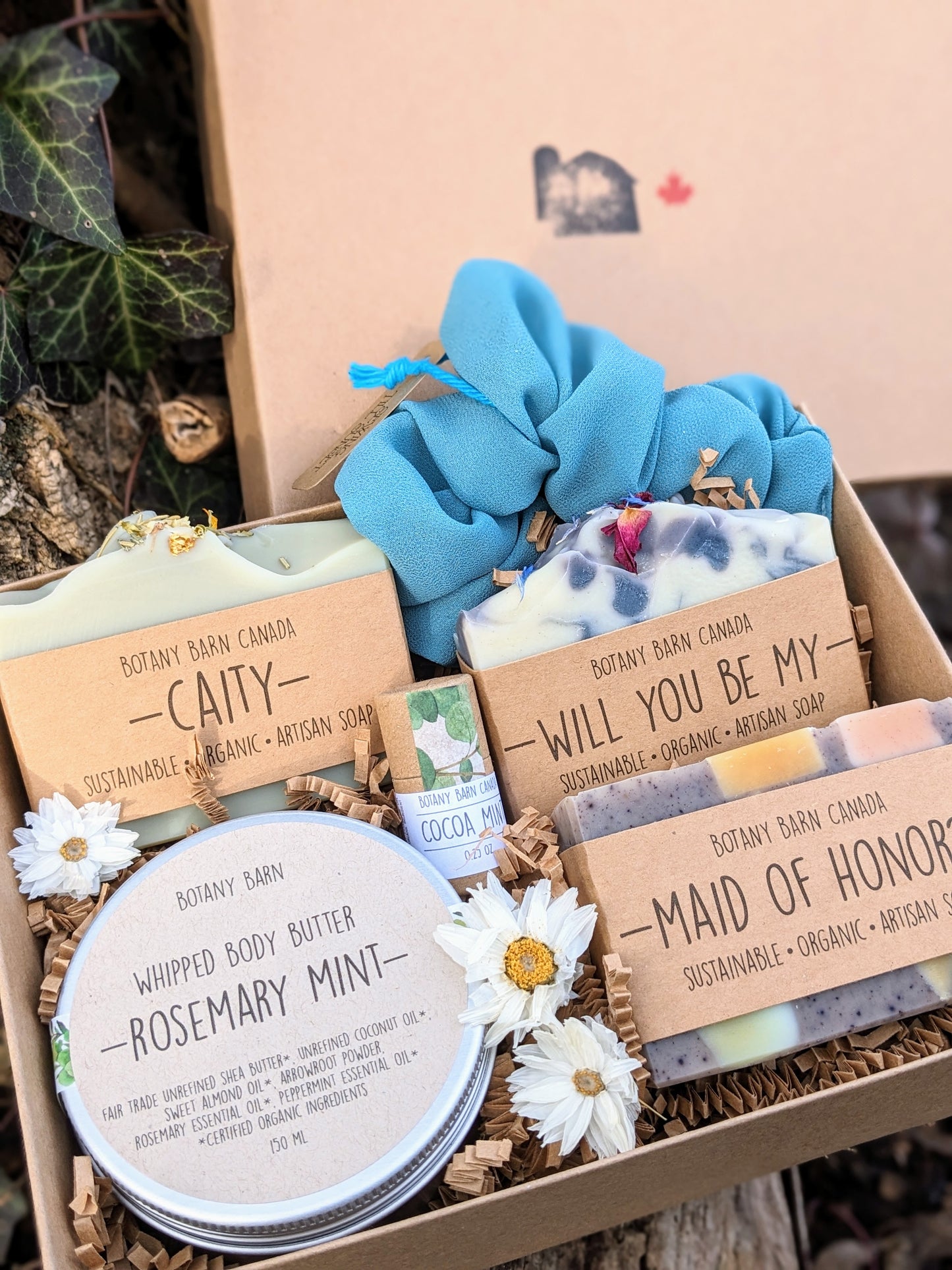 A gift set including handmade soaps, body butter, lip balm, and a scrunchie, packaged in a kraft box with custom labels and tied with a bow.