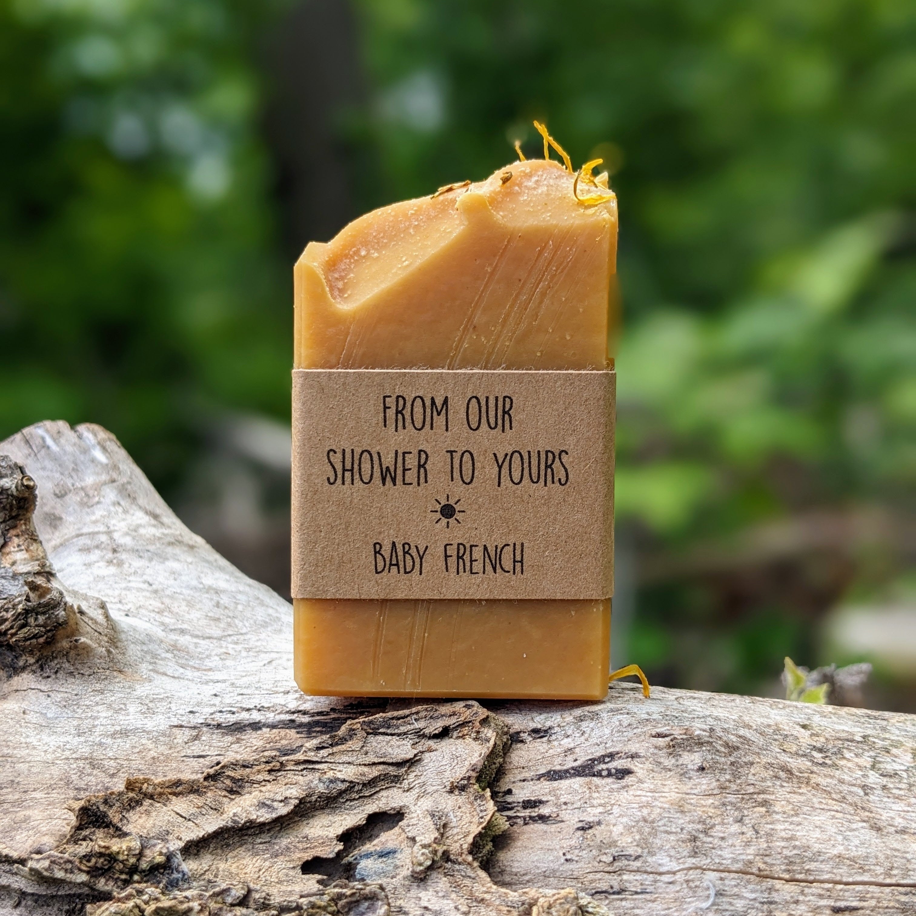 A yellow handmade soap bar with custom labels reading "from our shower to yours" displayed in an outdoor setting