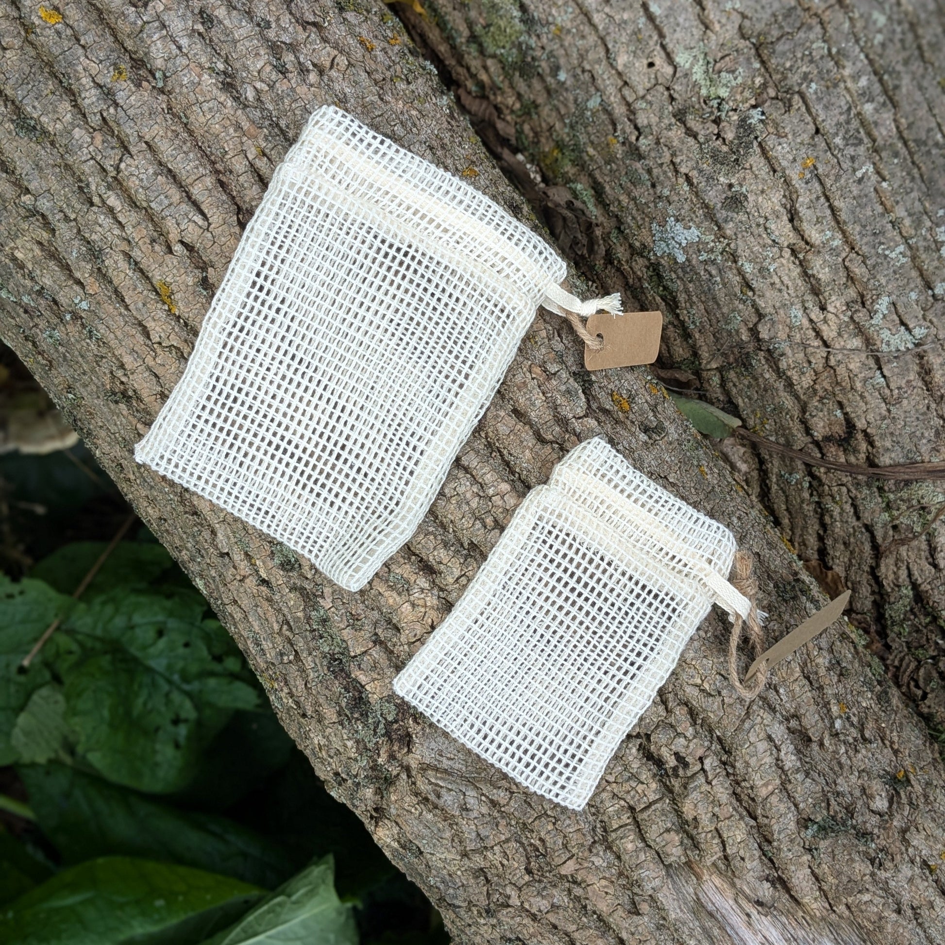 Two cotton mesh bags, one large and one small, displayed on a log in an outdoor setting.