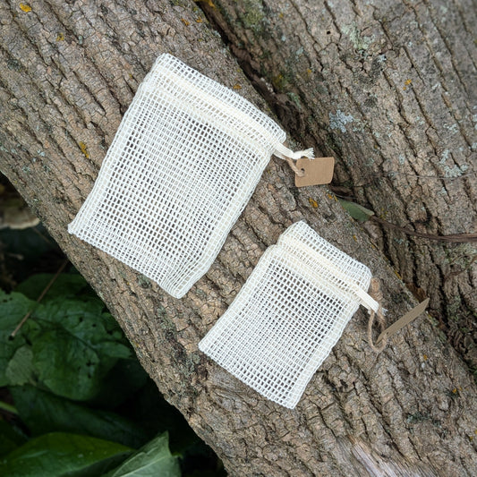 Two cotton mesh bags, one large and one small, displayed on a log in an outdoor setting.