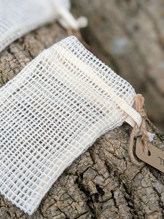 A small white organic cotton soap saver bag with a drawstring, displayed on a natural textured surface.
