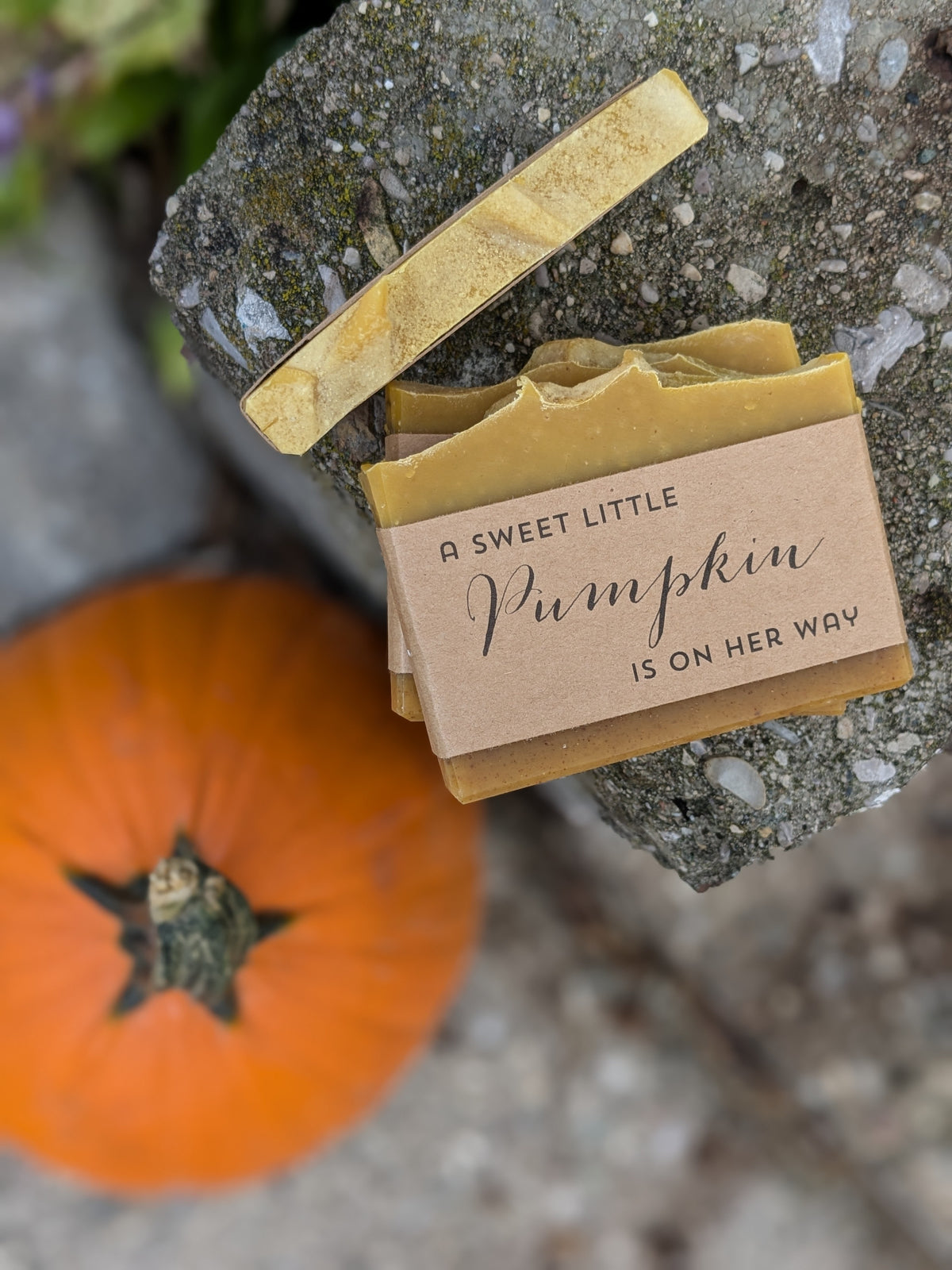 Handmade soap bars next to a pumpkin wrapped in brown kraft paper with text 'a sweet little pumpkin is on her way'.