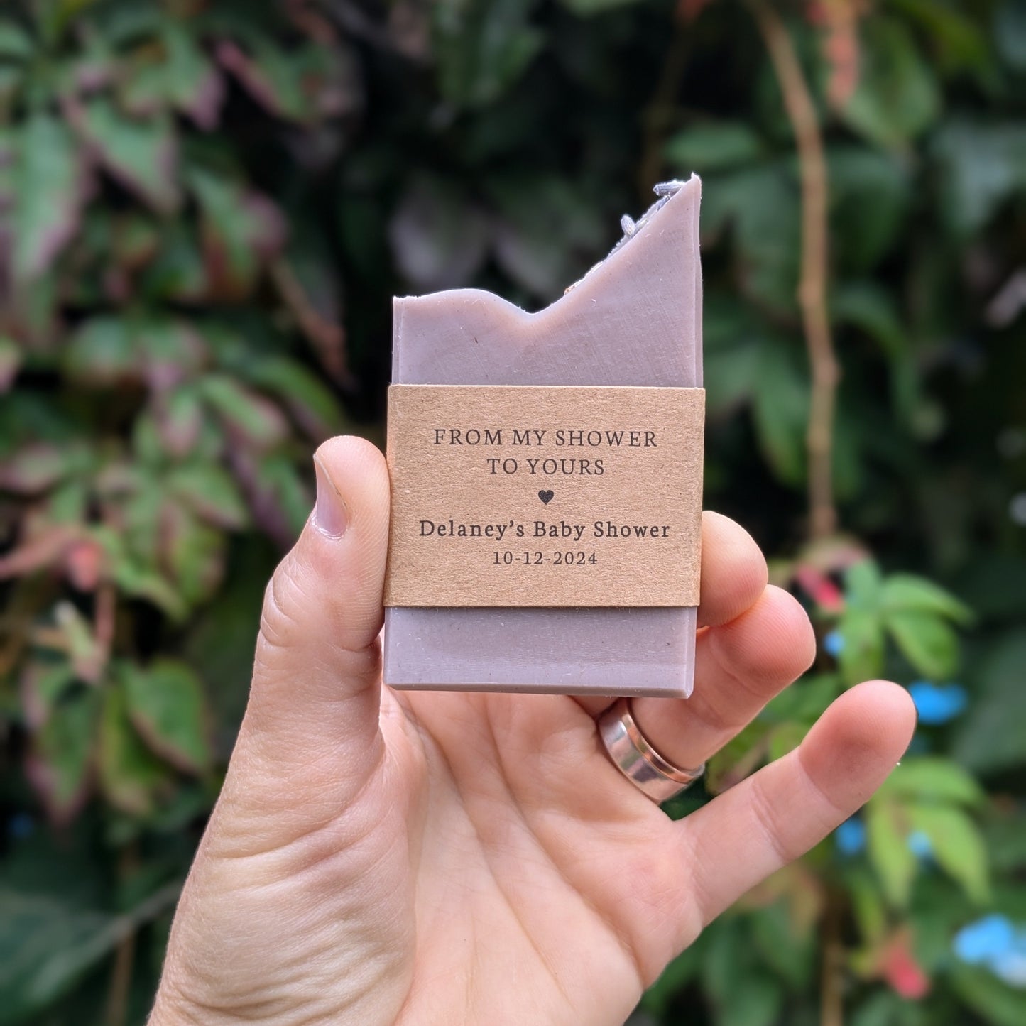 A hand holding a purple soap bar with custom labels reading "from my shower to yours" in an outdoor setting