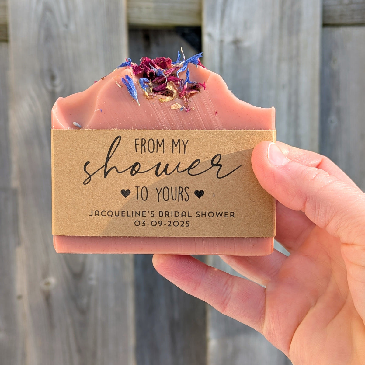 Hand holding a pink soap bar with a decorative label against a wooden background