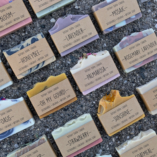 A variety of handcrafted soap bars with different colors and scents, labeled with names such as Aurora Borealis, Bloom, and Lavender, among others. The bars are placed on a neutral surface, showcasing their natural textures and colors.
