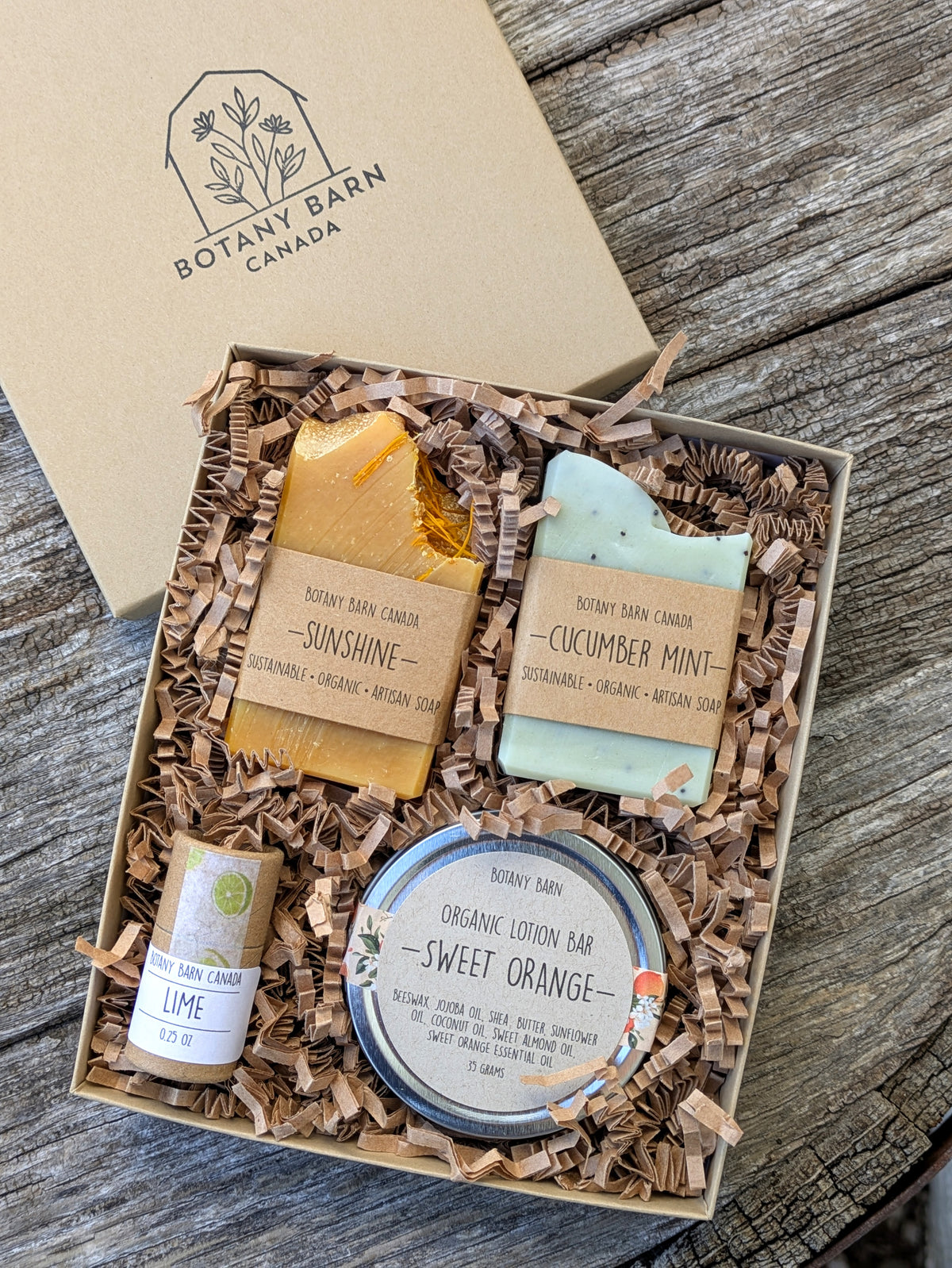 A gift box containing a variety of eco-friendly personal care items including mini soap bars, a lotion bar, and lip balm, all displayed on a bed of shredded paper filling.