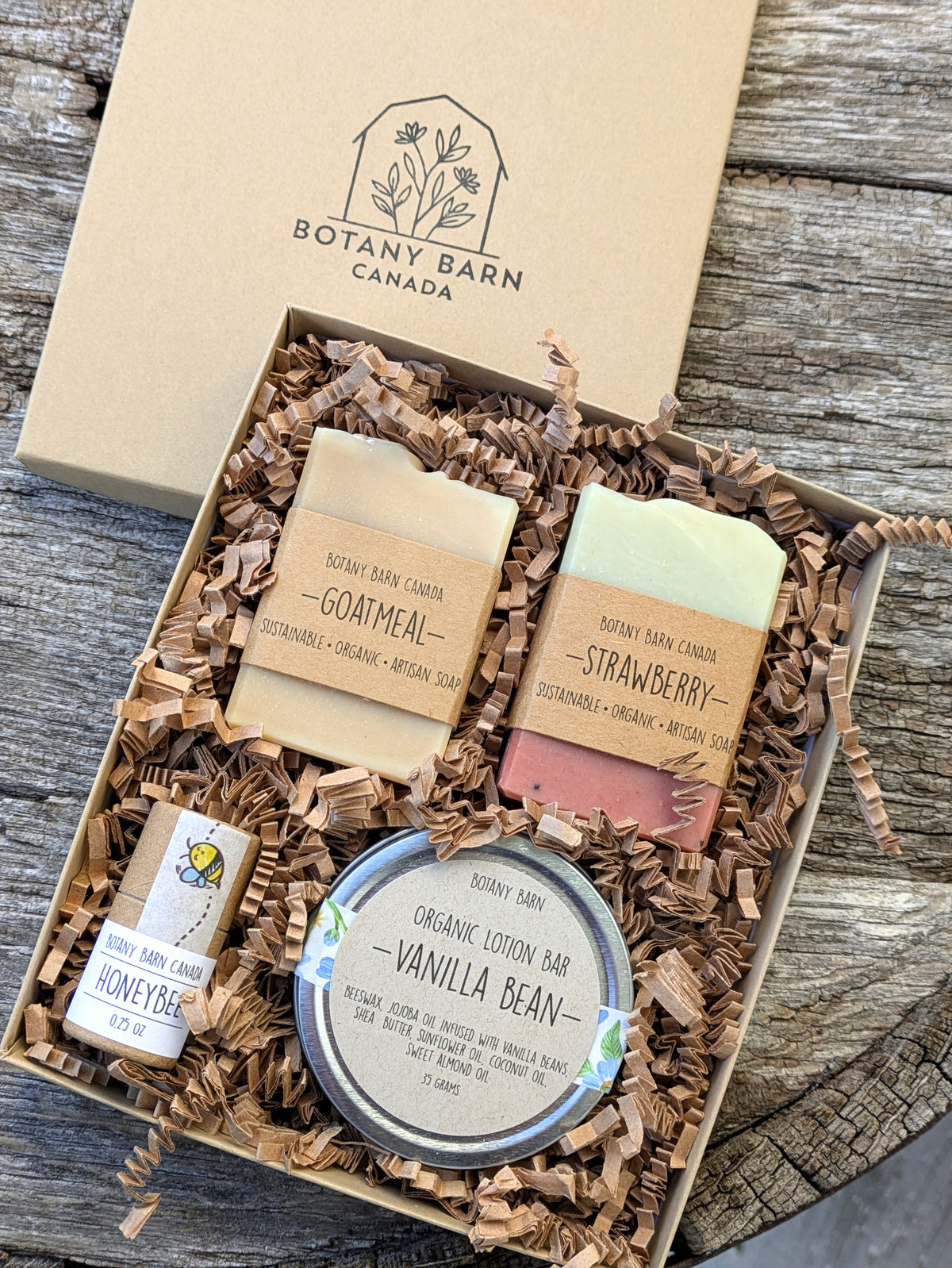A gift box containing a variety of eco-friendly personal care items including mini soap bars, a lotion bar, and lip balm, all displayed on a bed of shredded paper filling.