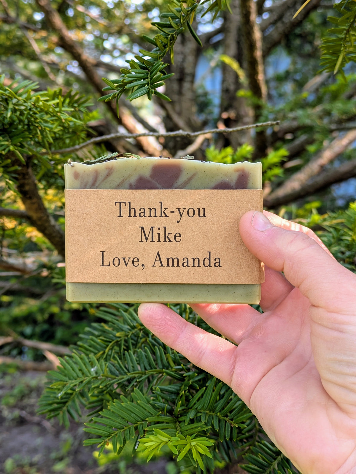 Hand holding a bar of soap with a personalized message against a natural background