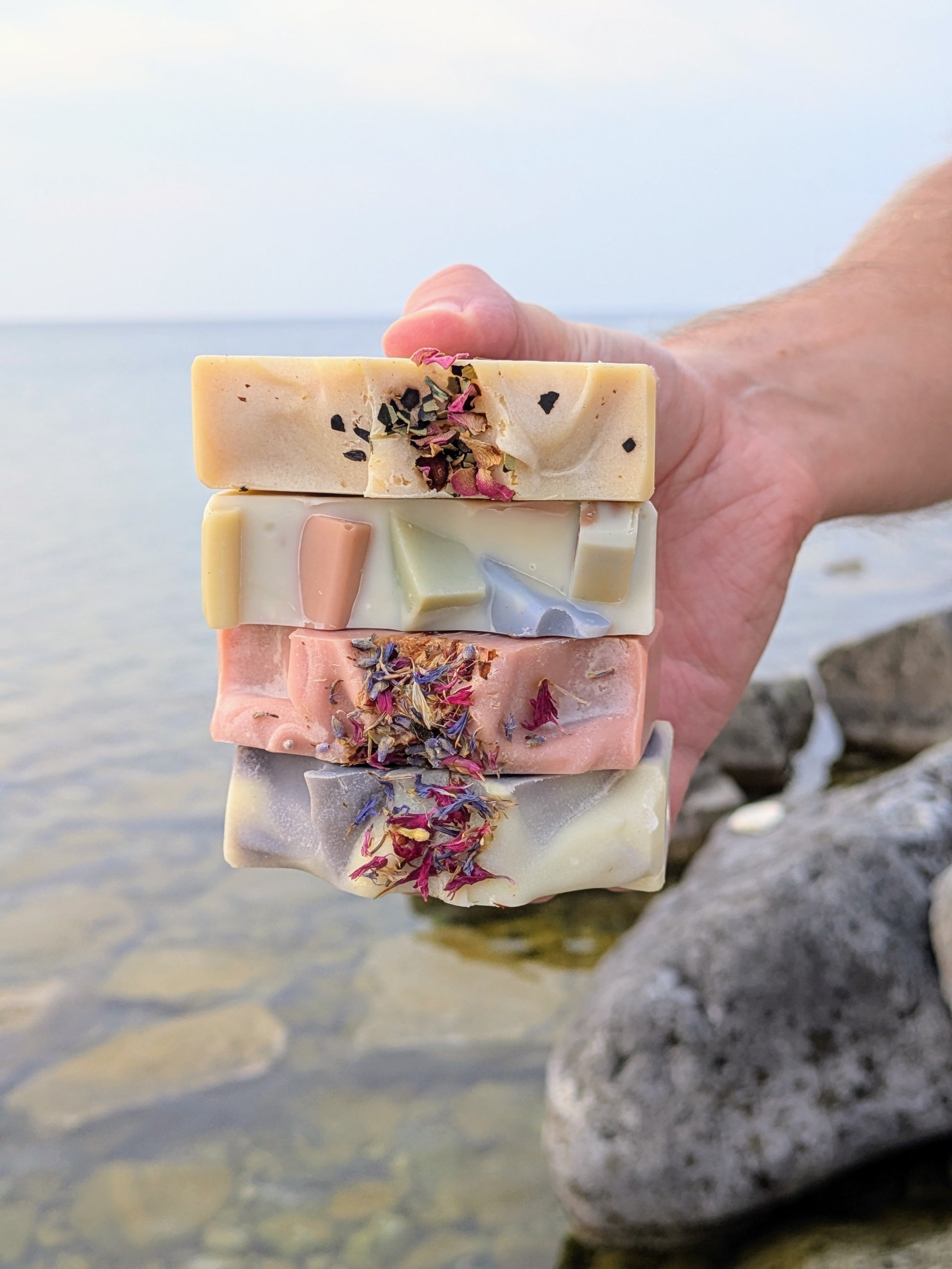 Hand holding three layered soap bars with natural ingredients against a natural background