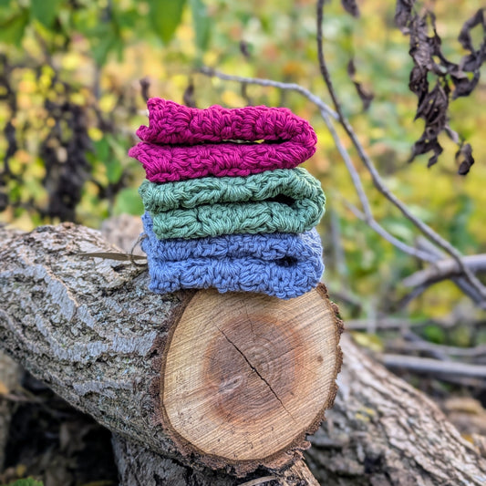Stack of colorful knitted washcloths on a wooden log with a natural background