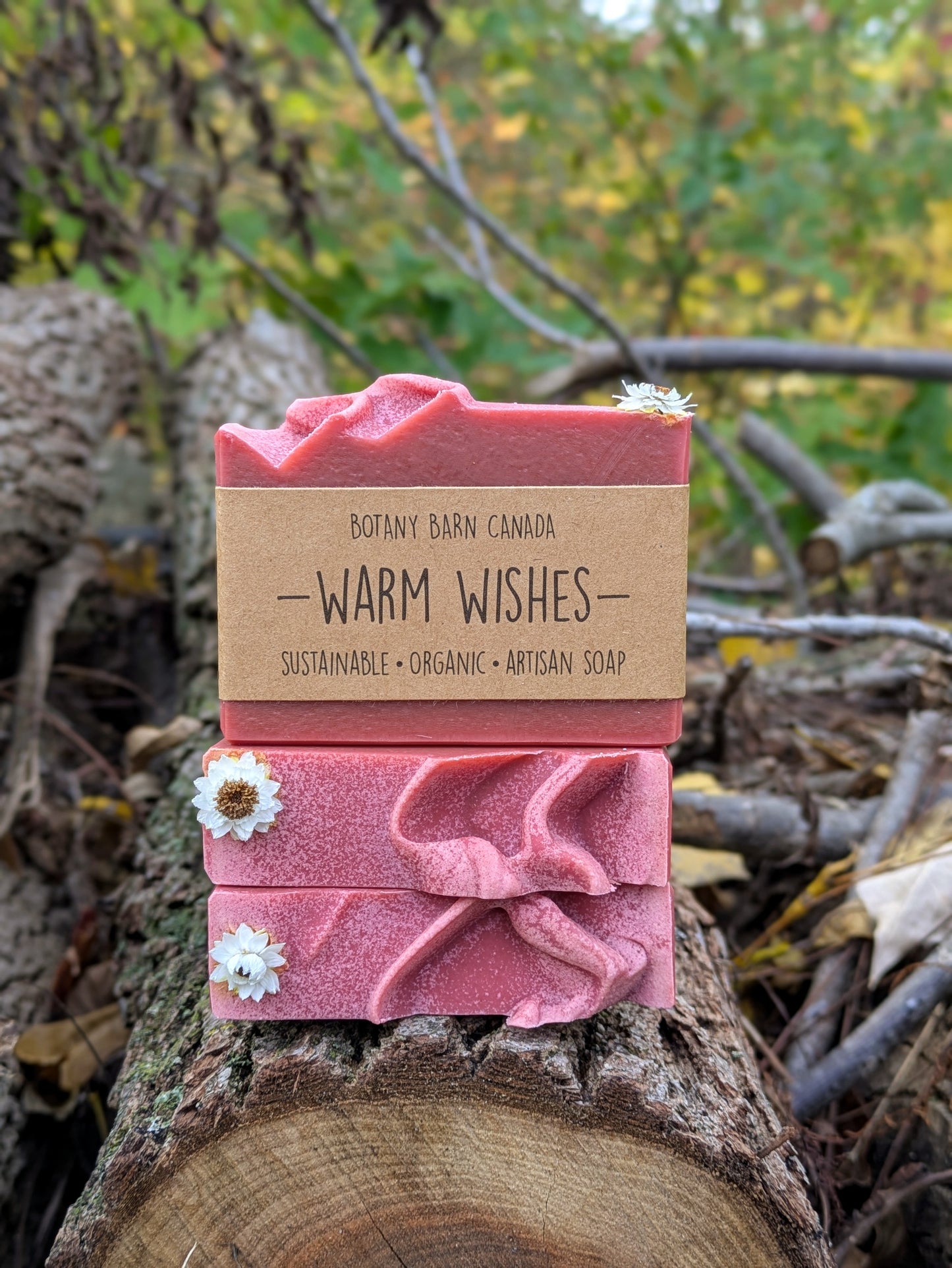Two red soap bars with a brown product label on a wooden log against a natural background