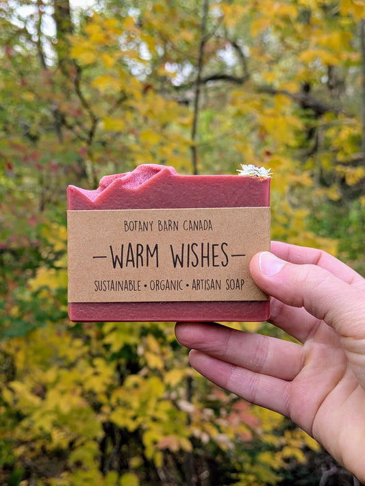 Bar of soap with a 'Warm Wishes' label held in front of a blurred natural background
