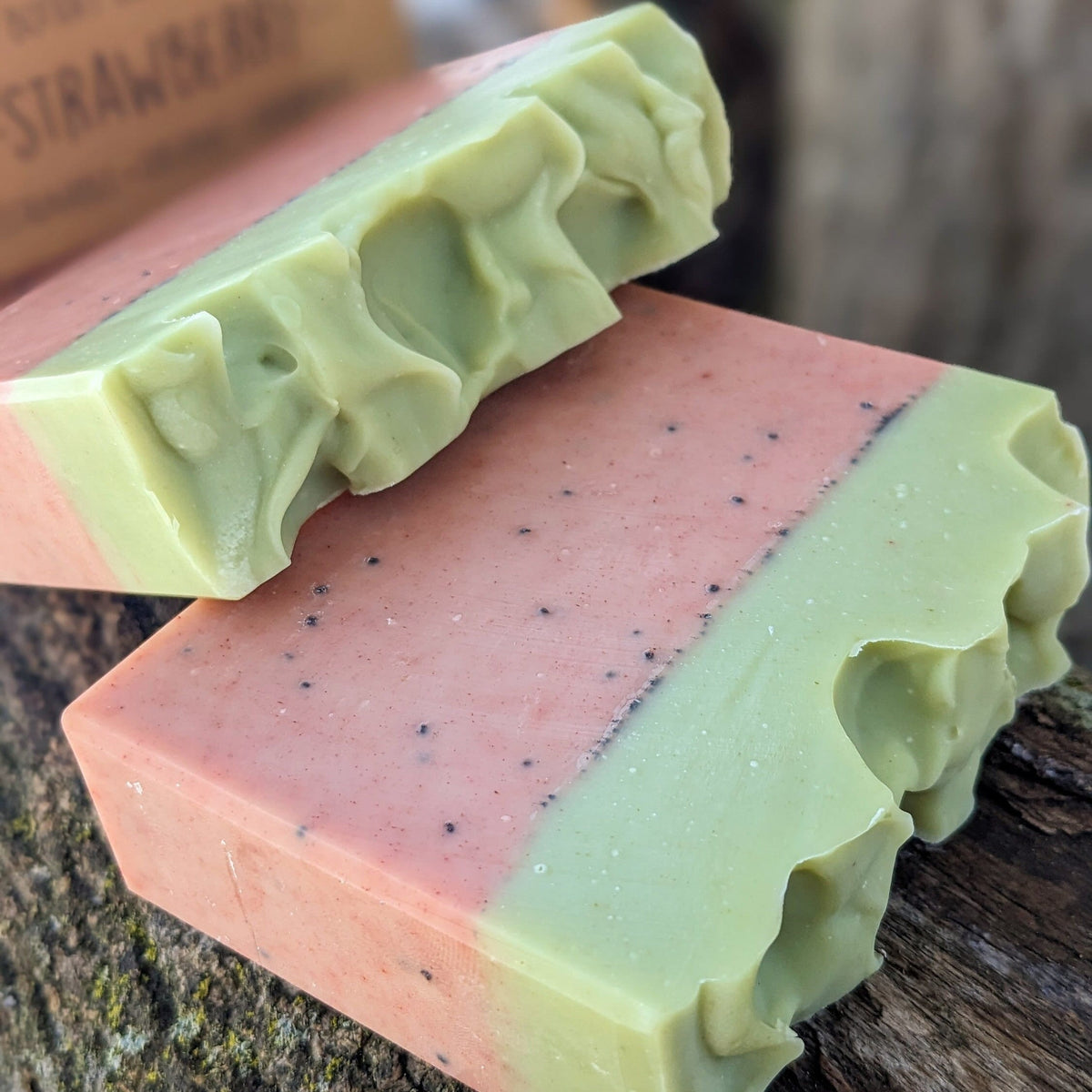 Two bars of soap with a strawberry theme on a wooden surface
