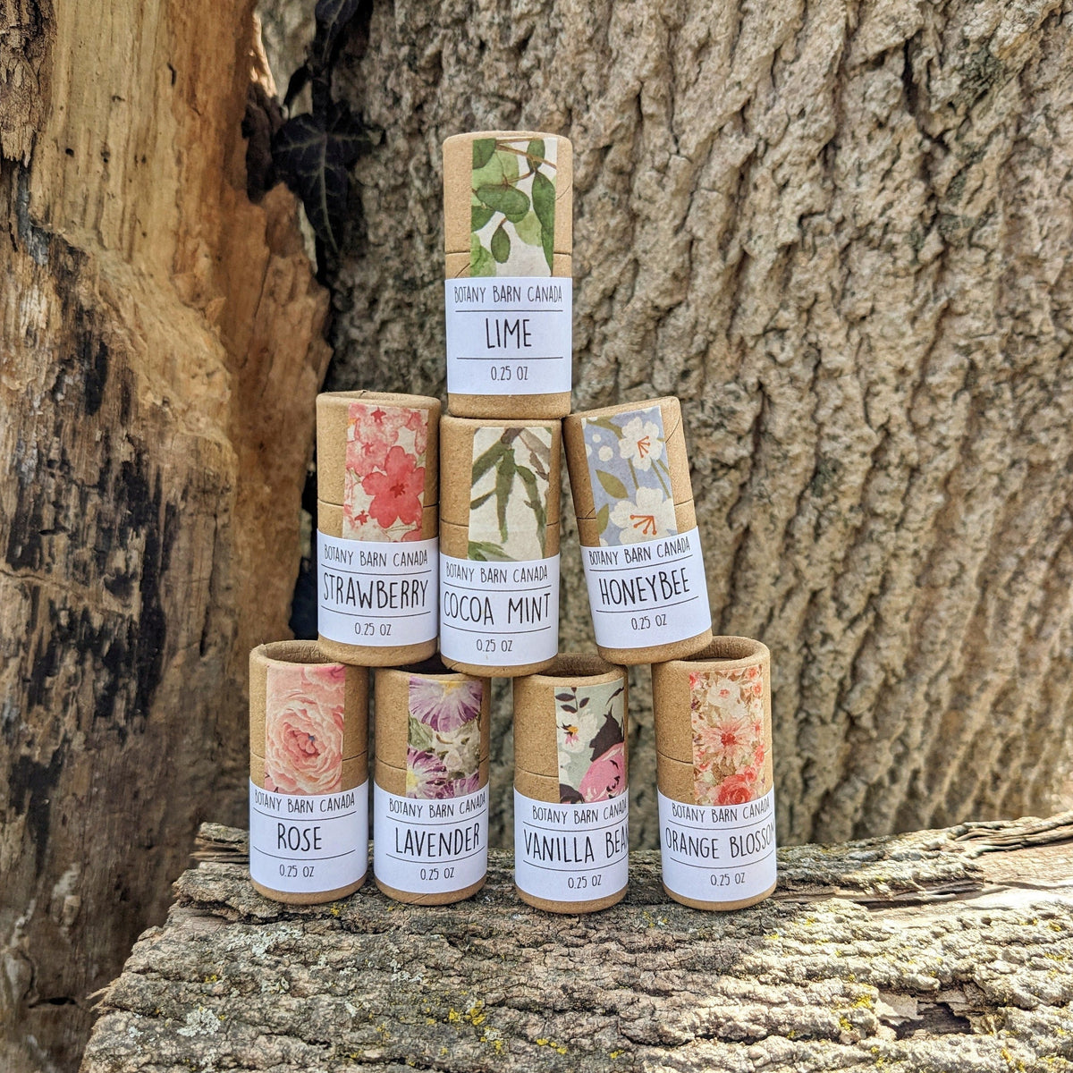 Eight lip balms tubes with colourful labels stacked on a log