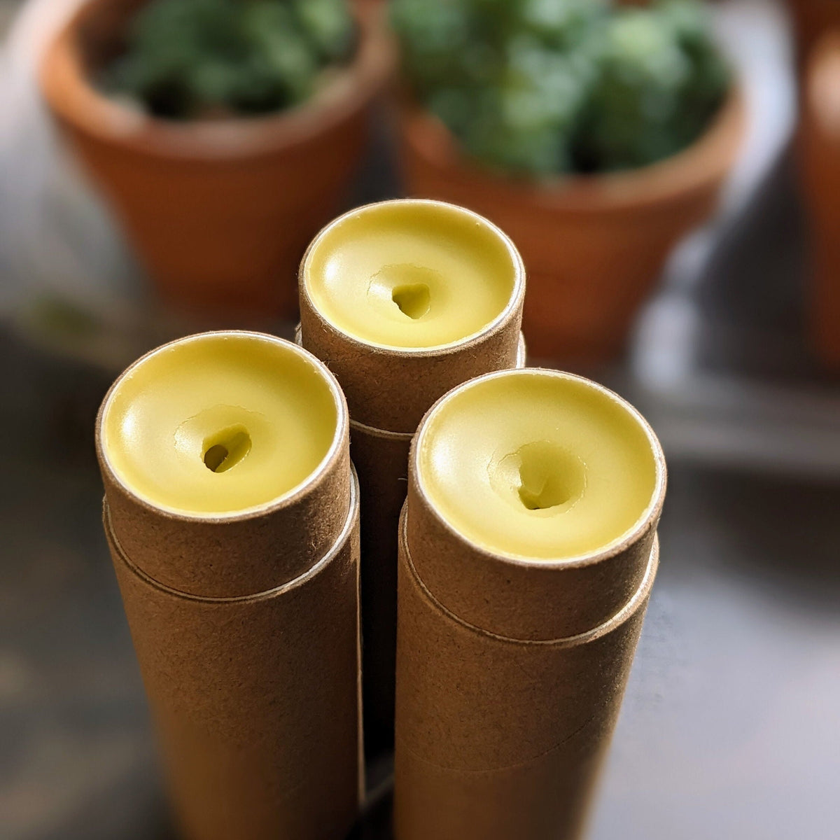 Three cardboard tubes, open and displaying the solid lotion inside the tube, yellow colour from natural beeswax