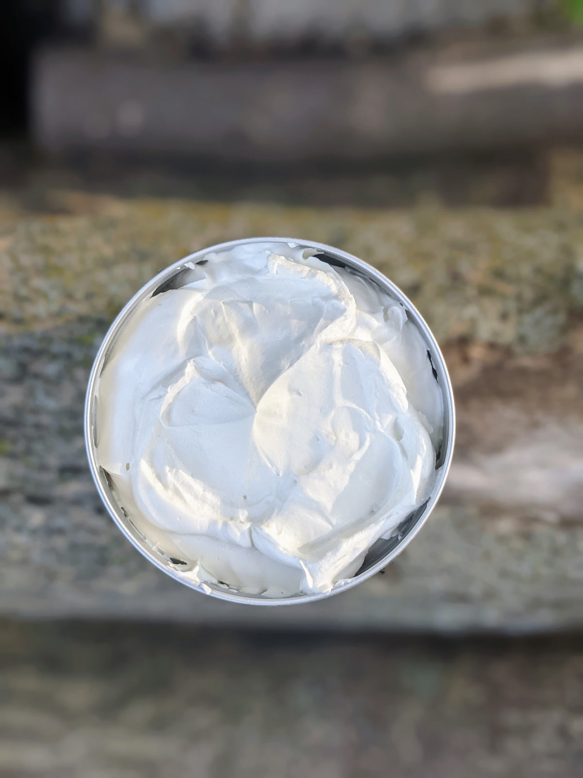 A container of whipped body butter is open, with the product inside visible as a creamy white substance.