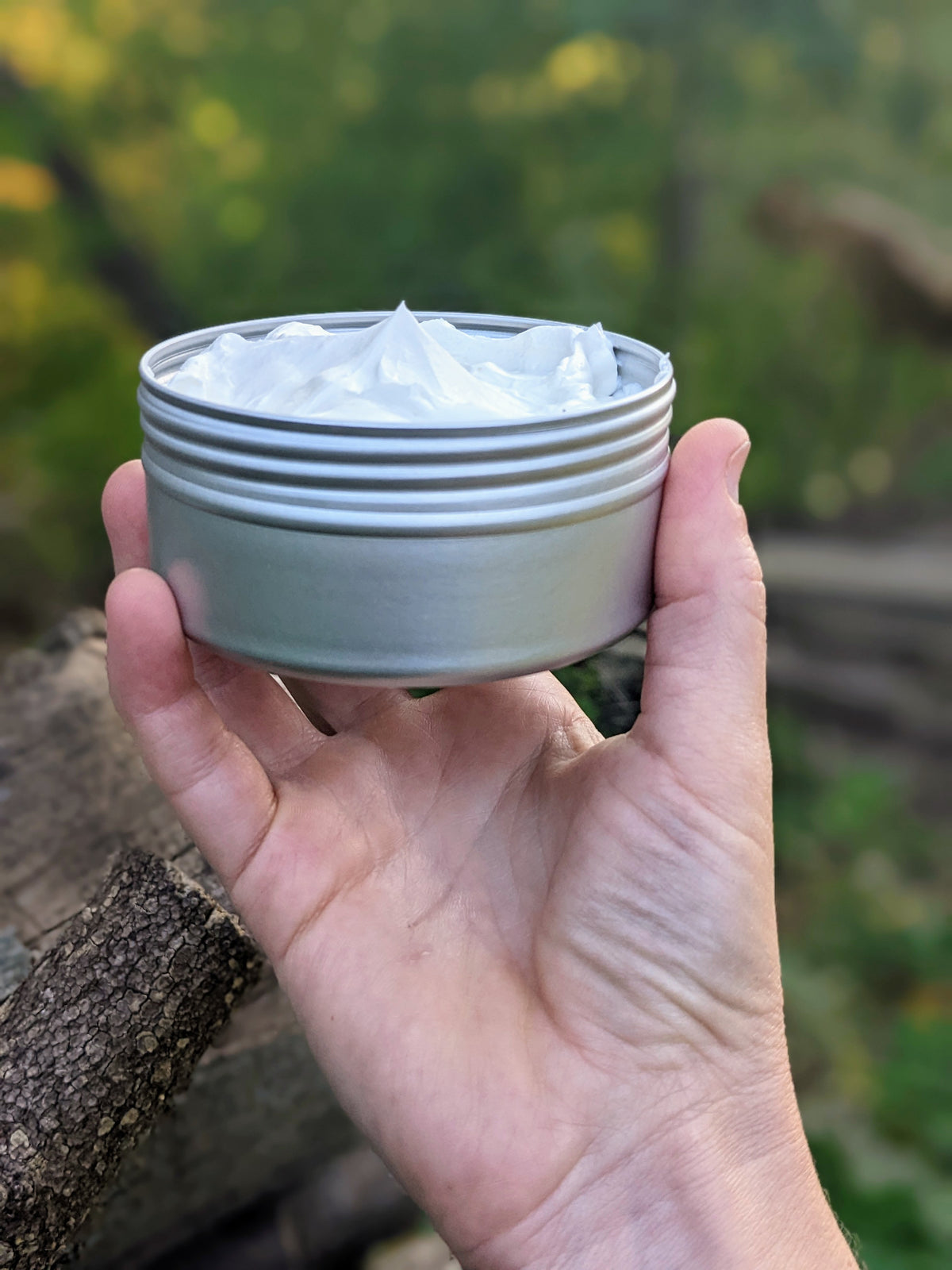 An open tin of whipped body butter, held in a hand