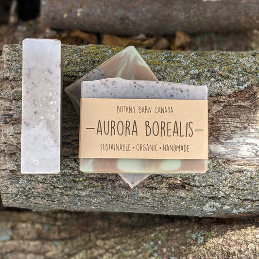 Bars of handmade artisan soap, top and front view. The soap is coloured purple, green & brown, swirled together. A brown label reads the name of the company, Botany Barn Canada and the name of the soap, Aurora Borealis.