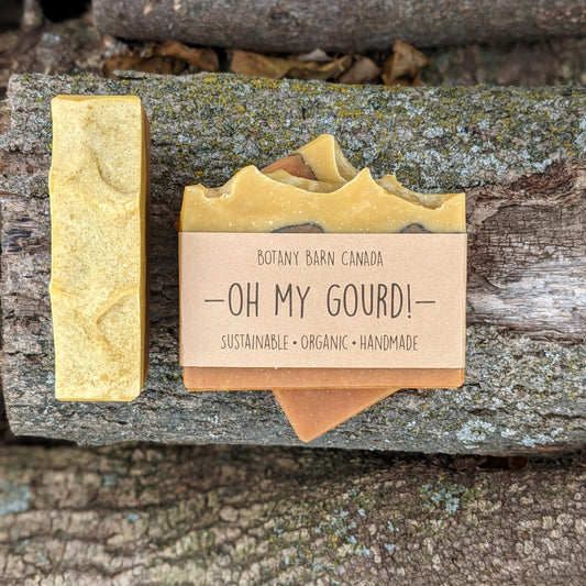 Bars of handmade artisan soap, top and front view. The soap is coloured 2 shades of orange. A brown label reads the name of the company, Botany Barn Canada and the name of the soap, Oh My Gourd.