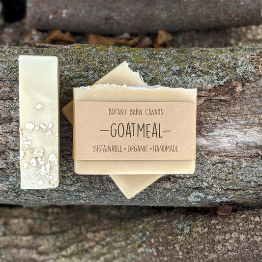 Bars of handmade artisan soap, top and front view. The soap is light brown in colour and the top is decorated with oats. A brown label reads the name of the company, Botany Barn Canada and the name of the soap, Goatmeal.