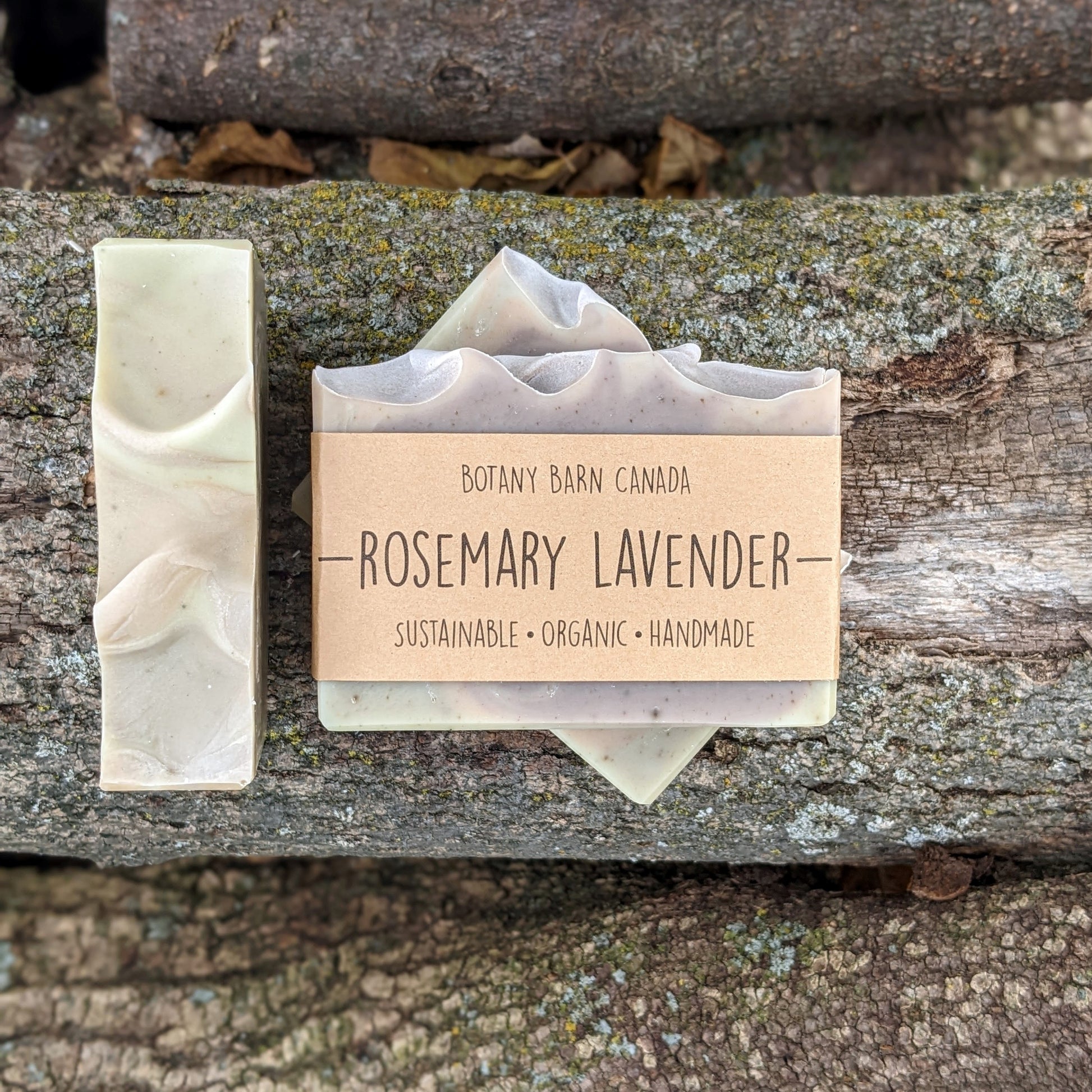 Bars of handmade artisan soap, top and front view. The soap is pink, purple & green in colour. A brown label reads the name of the company, Botany Barn Canada and the name of the soap, Rosemary Lavender.