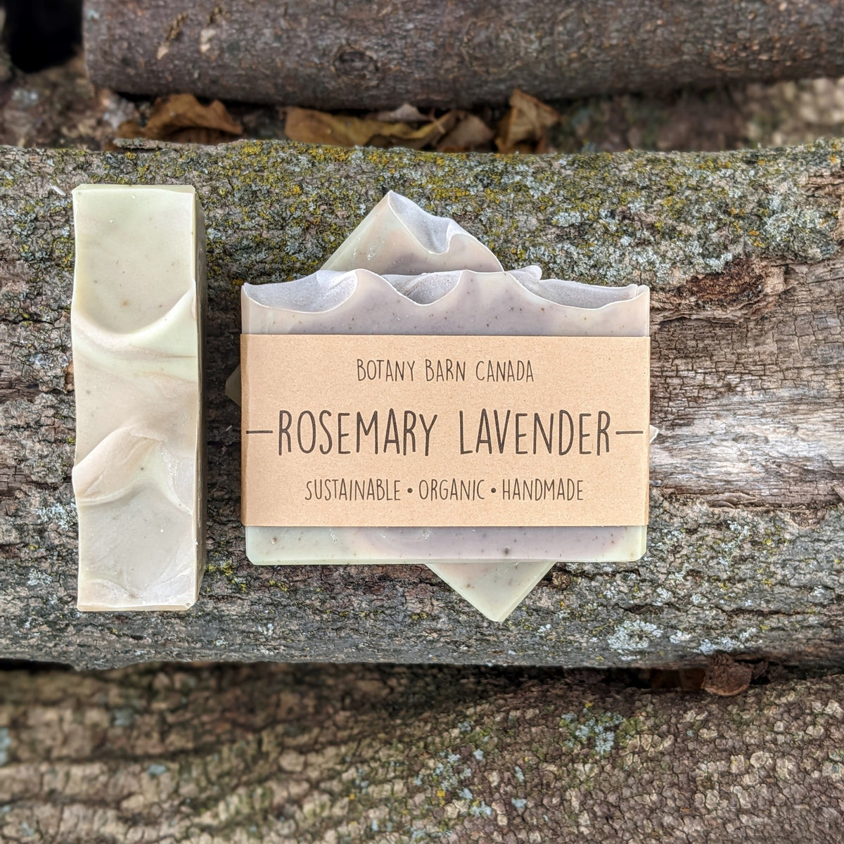 Bars of handmade artisan soap, top and front view. The soap is pink, purple & green in colour. A brown label reads the name of the company, Botany Barn Canada and the name of the soap, Rosemary Lavender.