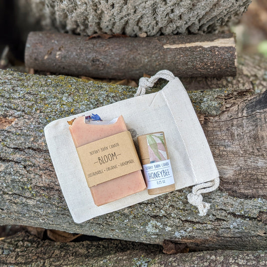 A mini soap bar and a tube of lip balm placed inside a beige muslin bag, set against a rustic wooden background.