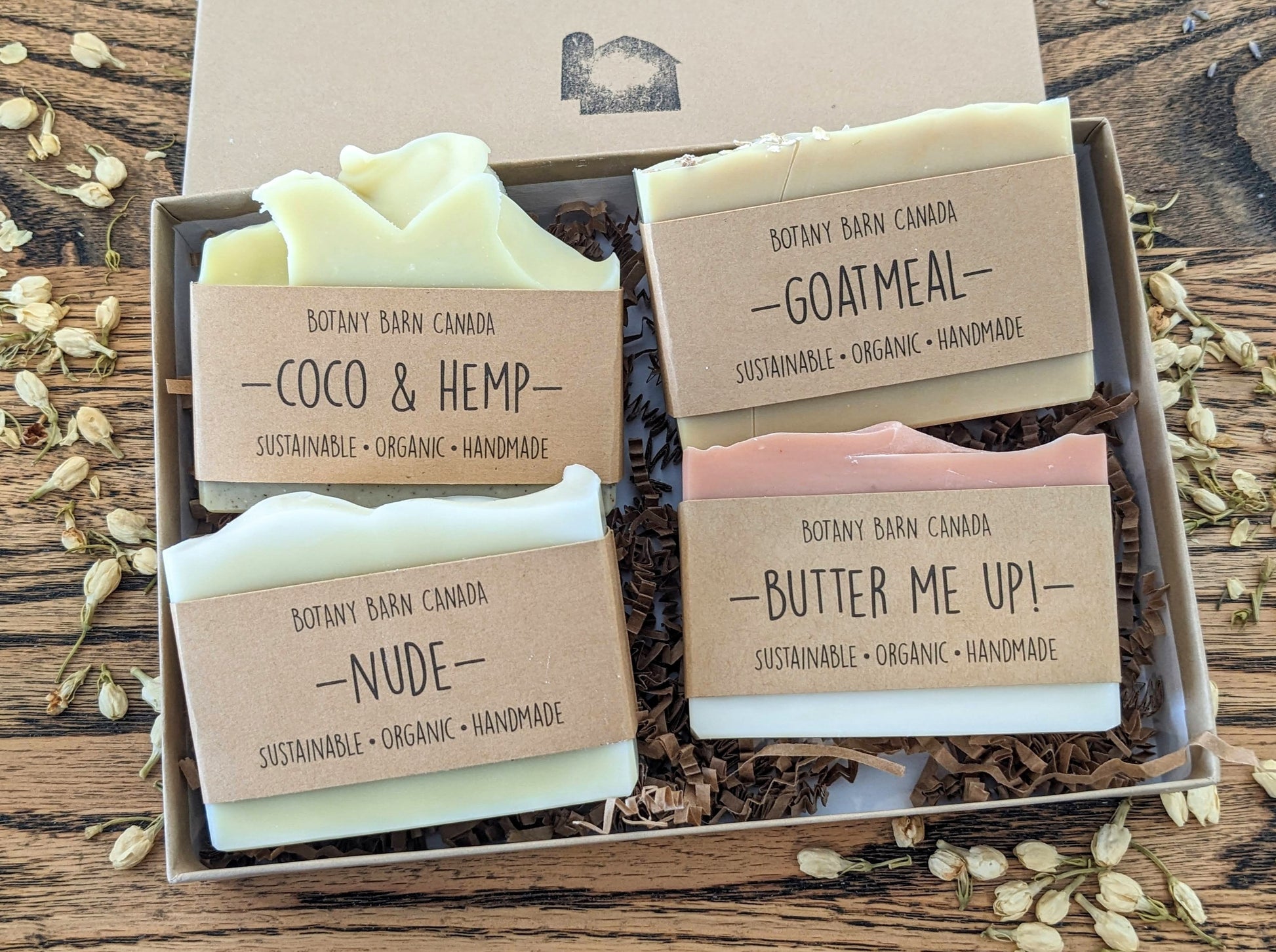 A set of four bar soaps with different colors and scents, arranged in a kraft gift box, with labels indicating the soap name and type.