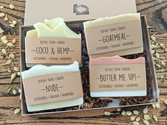 A set of four bar soaps with different colors and scents, arranged in a kraft gift box, with labels indicating the soap name and type.