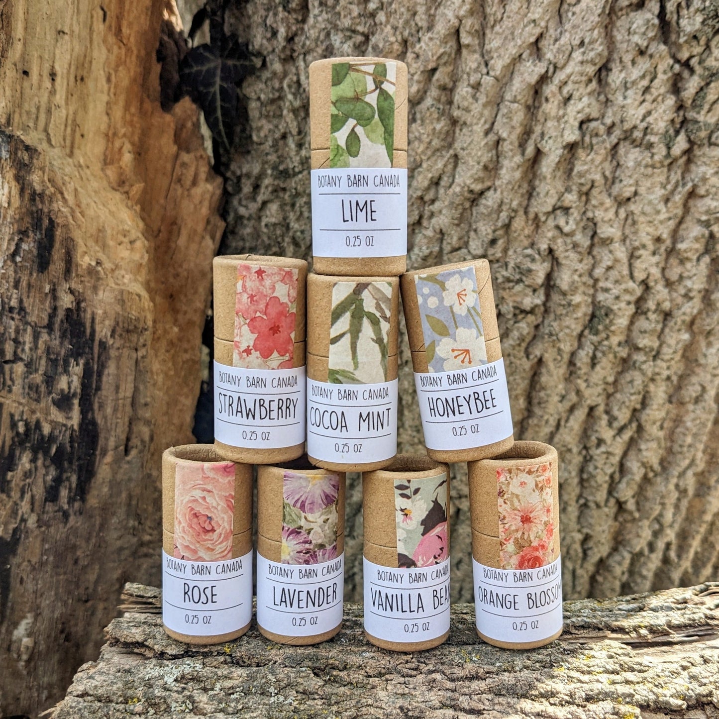 Eight lip balm tubes with colourful labels, stacked on a log