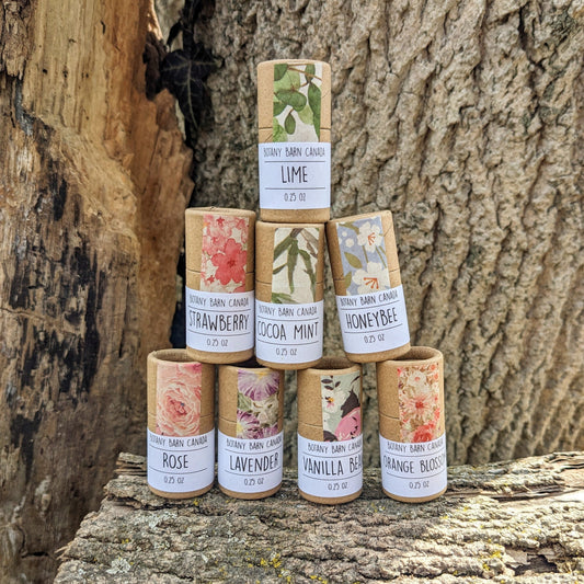 A collection of eight eco-friendly cardboard tubes of lip balm with various floral labels, displayed against a natural wood backdrop.