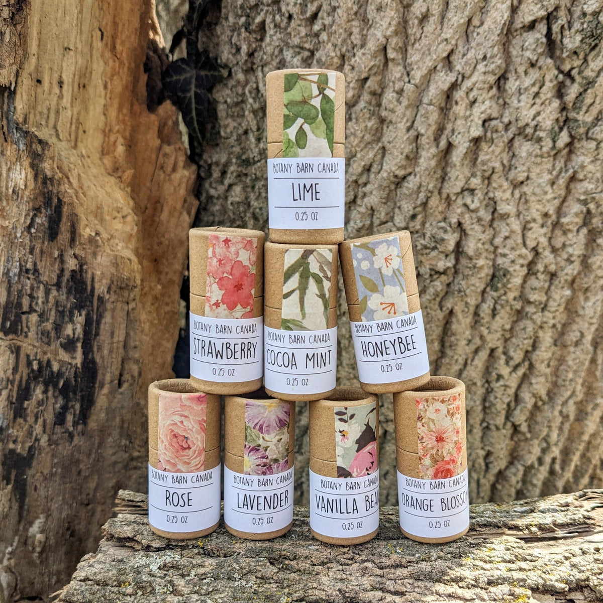 Eight lip balm tubes with colourful labels, stacked on a log
