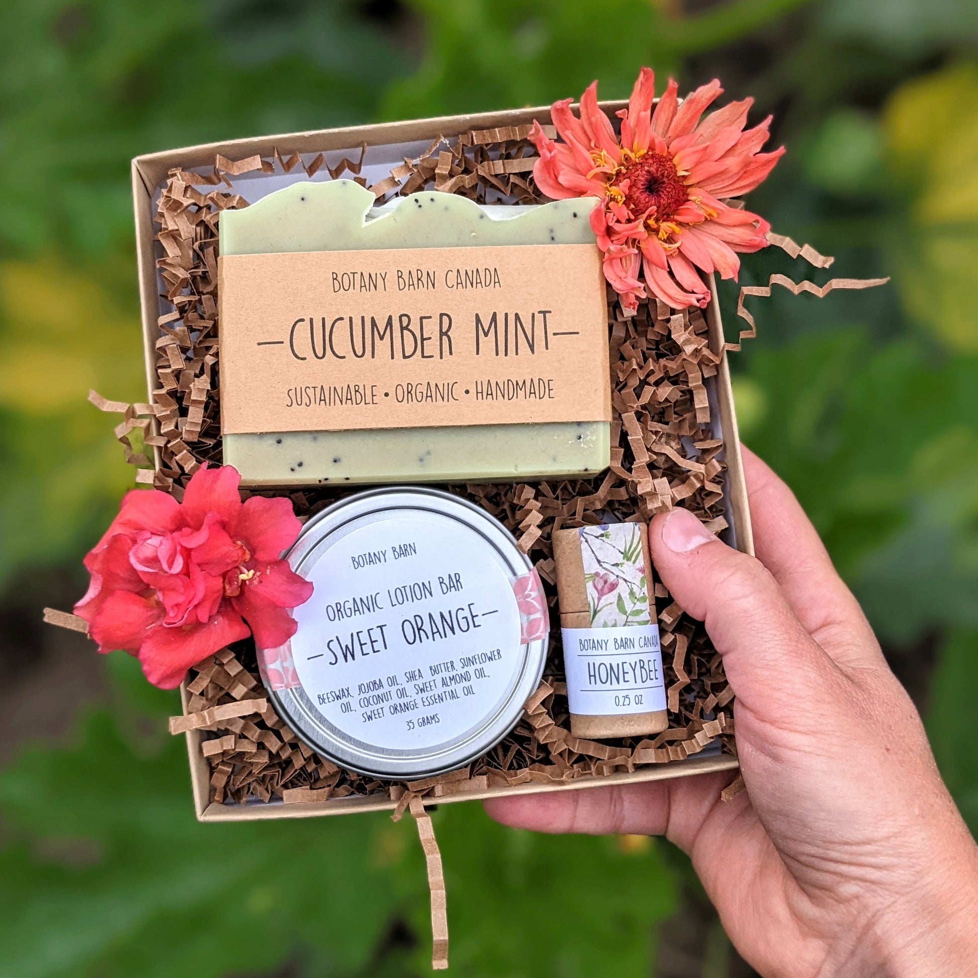 A custom gift box containing a bar of soap, a metal tin with lotion bar, and an eco-friendly tube of lip balm, all displayed with decorative flowers.