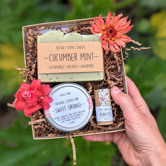 A custom gift box containing a bar of soap, a metal tin with lotion bar, and an eco-friendly tube of lip balm, all displayed with decorative flowers.