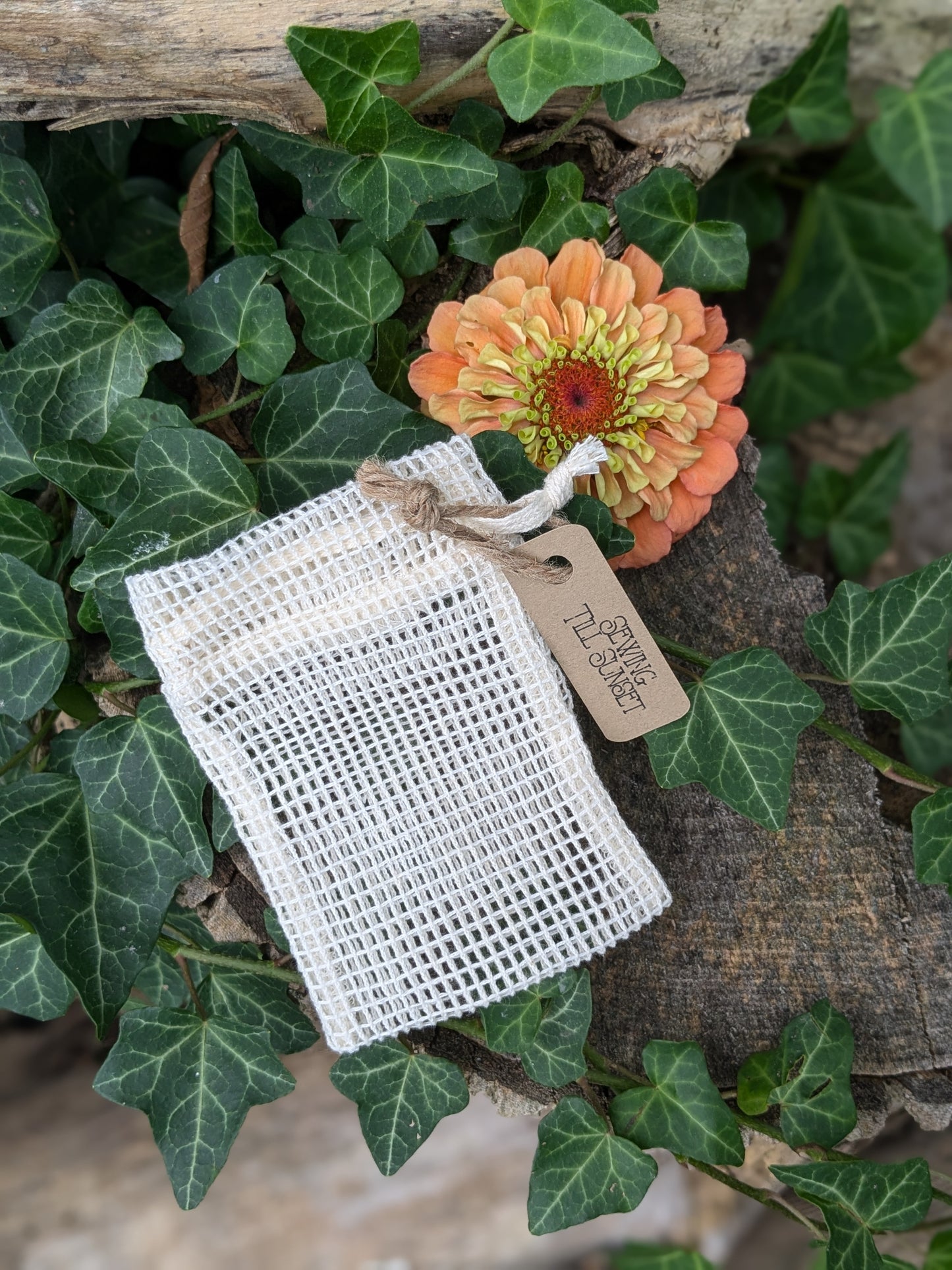 White mesh soap bag with a tag on green leaves and flowers
