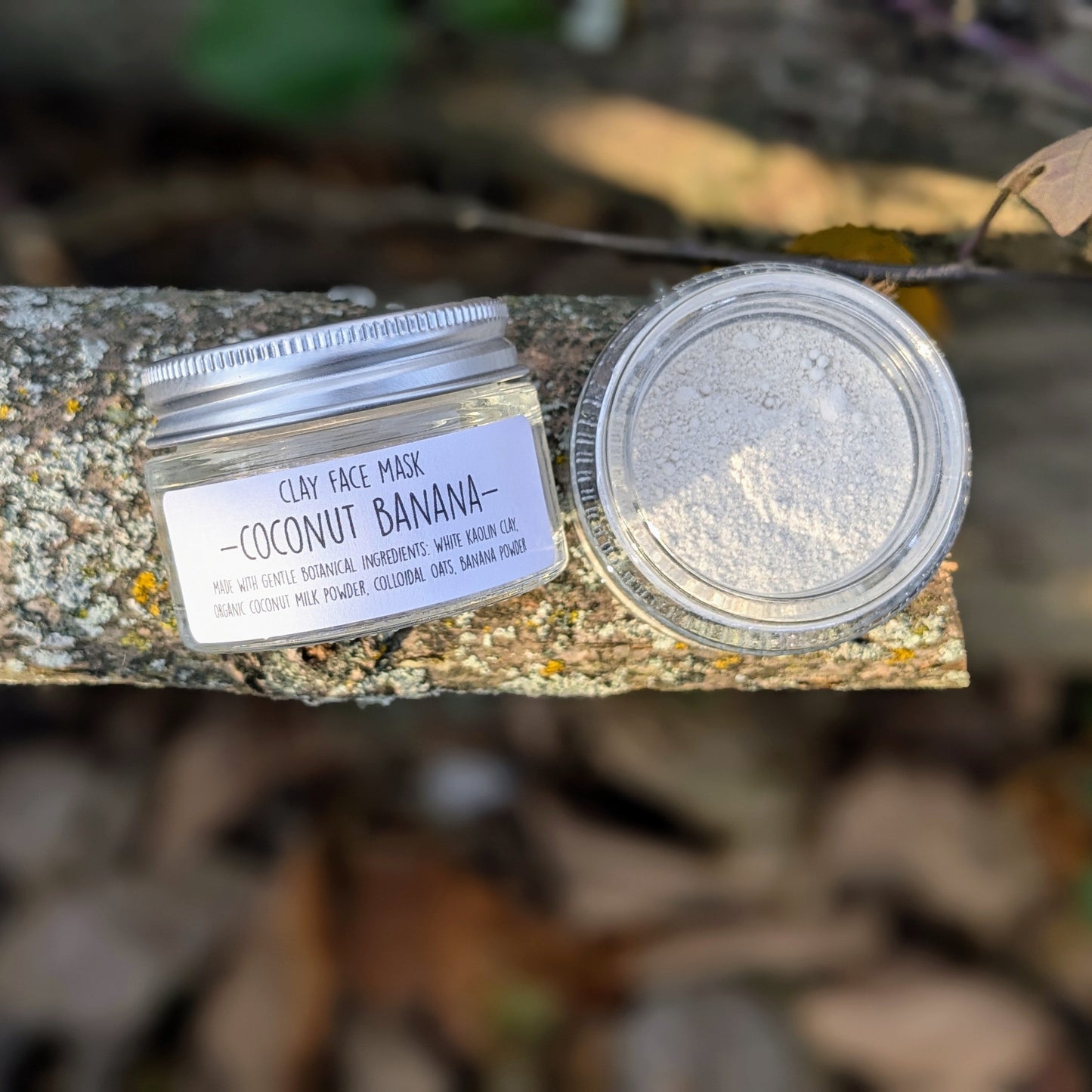 Jar of coconut banana clay face mask on a wooden surface with a blurred natural background