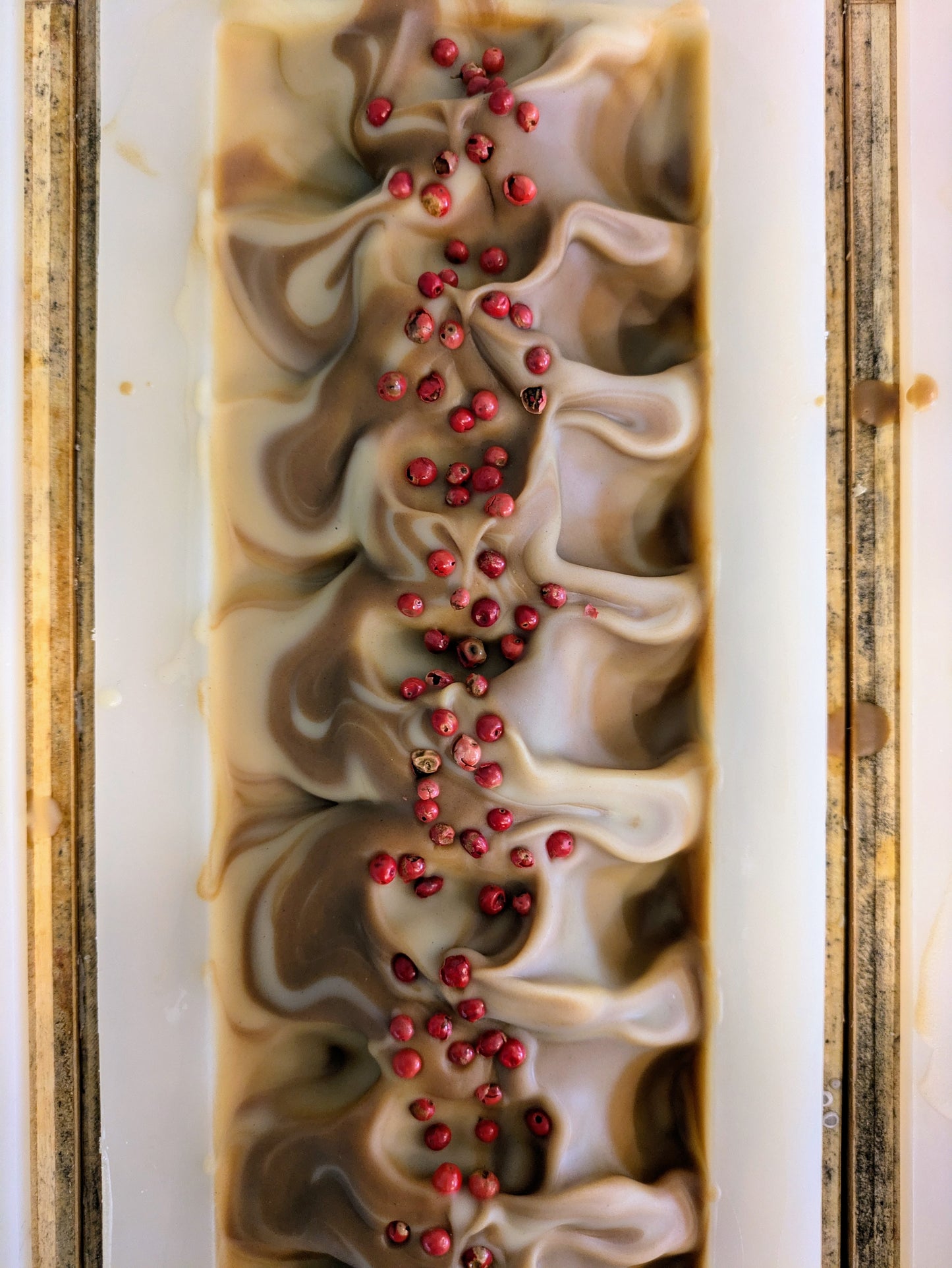 Top view of a loaf of soap with wavy pattern topped with red peppercorns