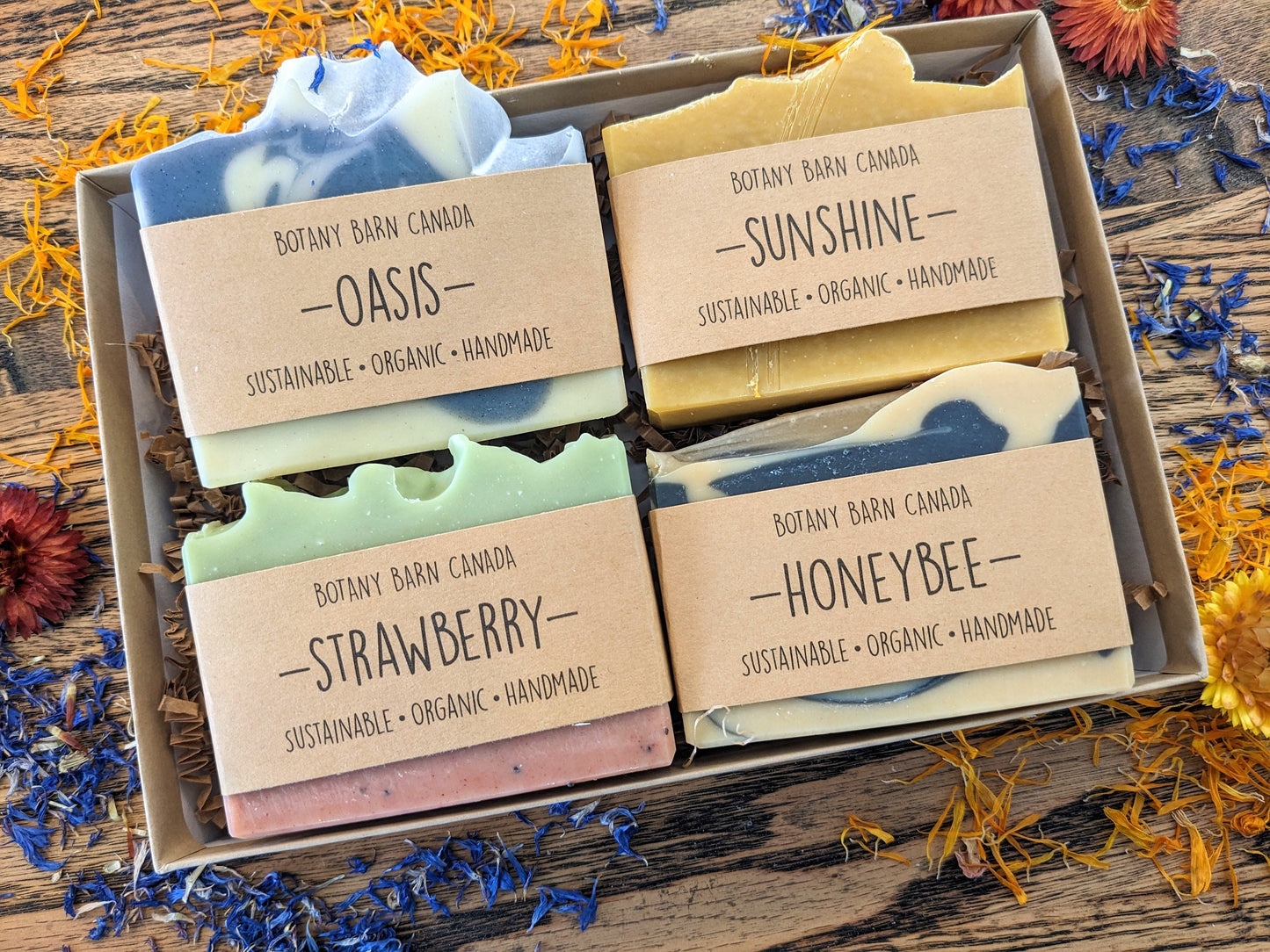 Box of Botany Barn Canada soaps with labels on a wooden surface with dried flowers.