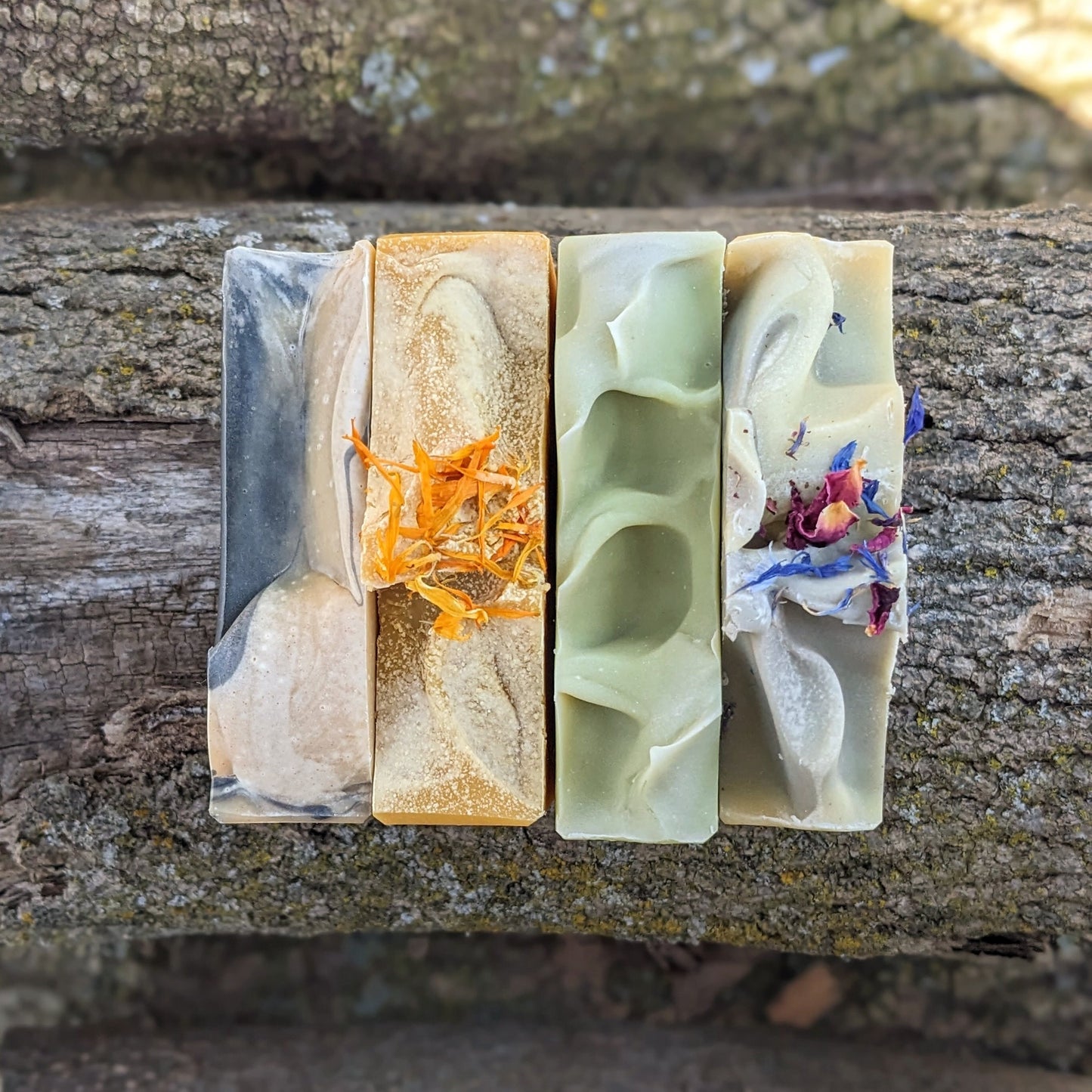 Four handmade soap bars with different textures and colors on a wooden surface
