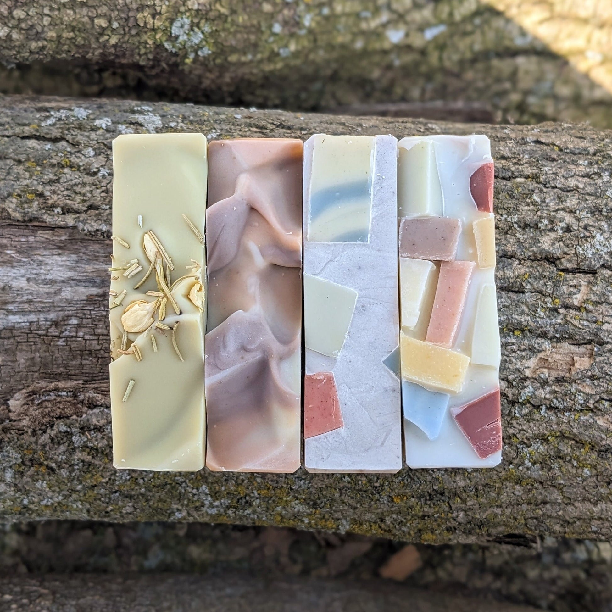 Four rectangular soap bars with different designs and colors on a wooden surface.