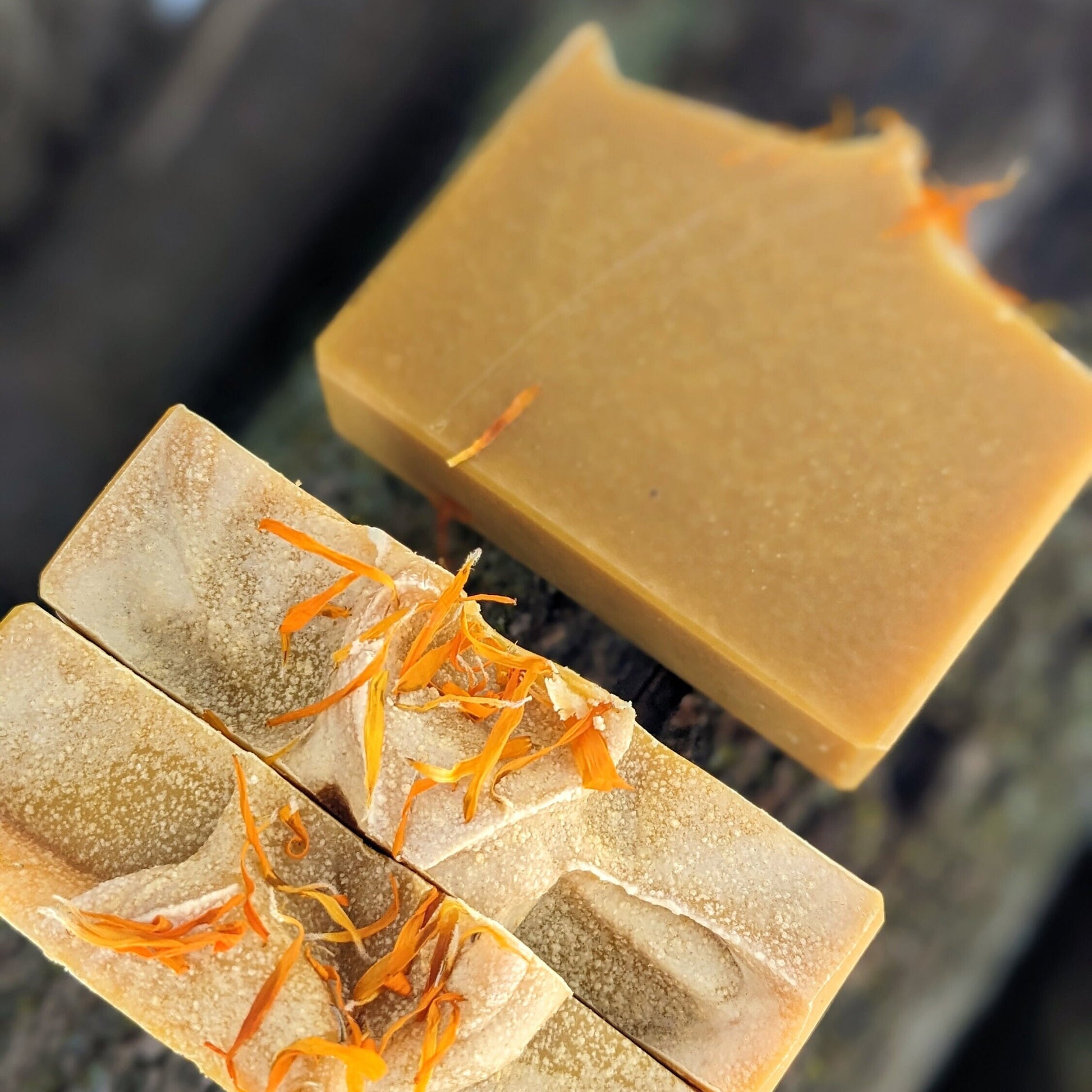 Two bars of soap with orange flowers on top on a dark background
