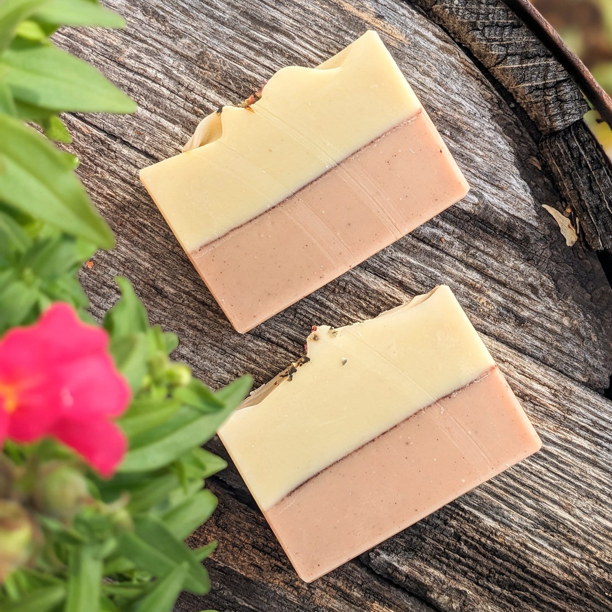 Two bars of pink and yellow soap, displayed on a wooden background